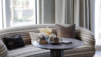 A modern living room with a striped sofa, a round table with a teapot, cup, and book, and a vase with a white flower.