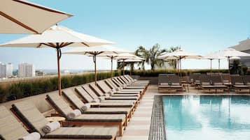 Ein Poolbereich mit Liegestühlen und Sonnenschirmen, ein Pool und eine Stadtkulisse im Hintergrund.