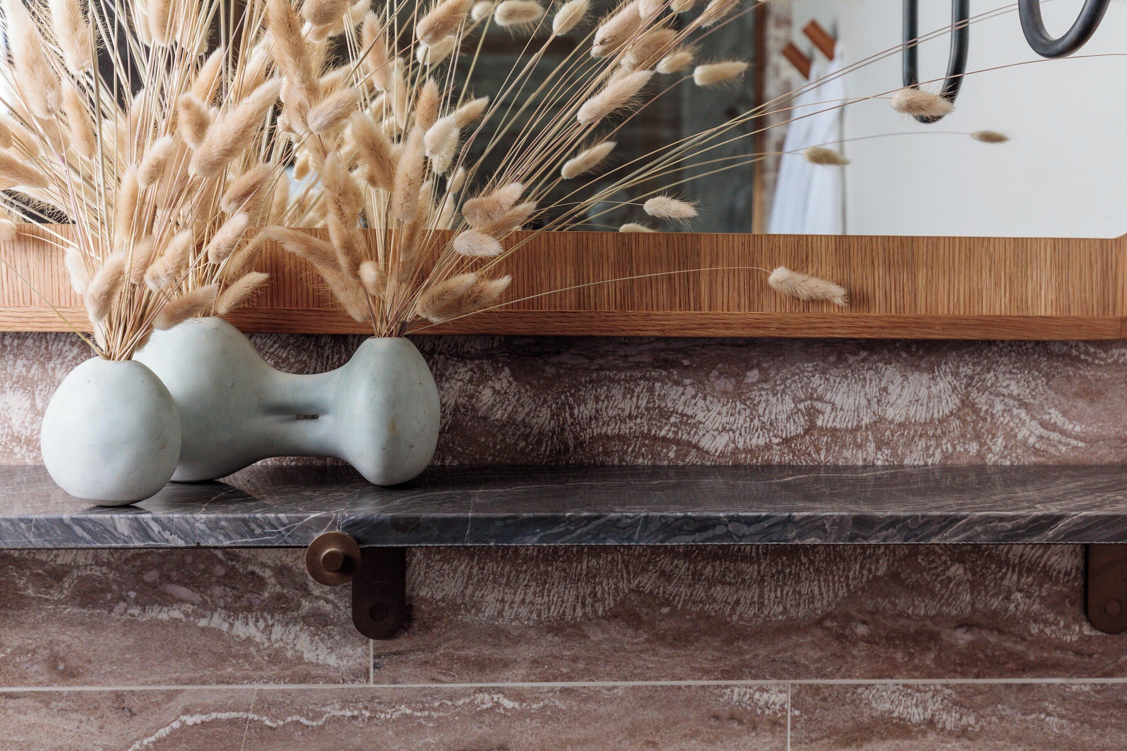 A marble countertop with a vase of dried pampas grass and a decorative bone-shaped object.
