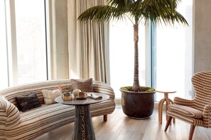A modern living room with a curved sofa, a round coffee table, a striped armchair, and a tall palm tree in a large planter. - Santa Monica Proper Hotel, a Member of Design Hotels (Santa Monica)
