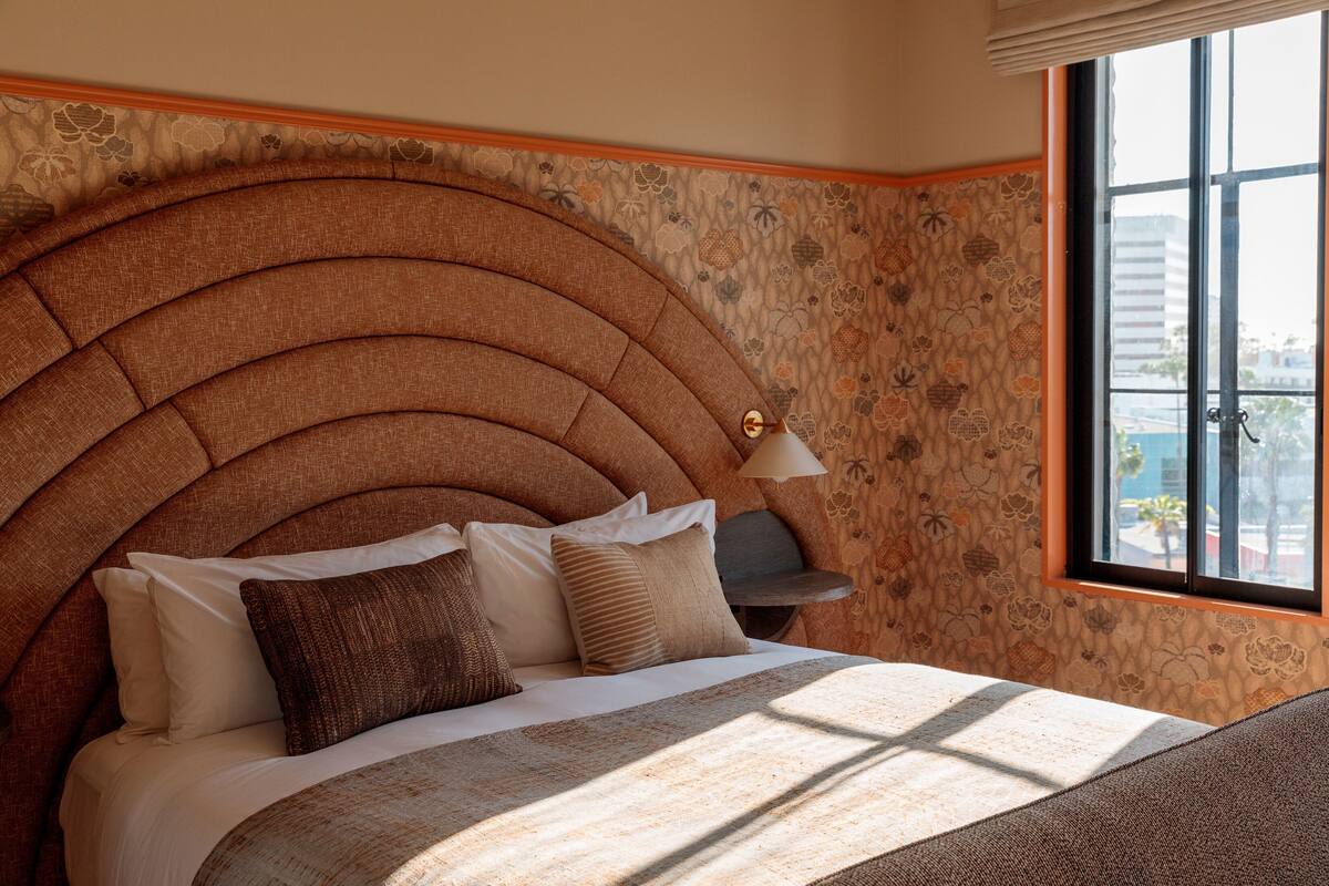 Una cama con cabecera curvada, una mesita de noche y una ventana con vistas a edificios.