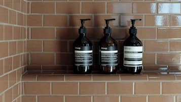 Three bottles of Aesop Classic Shampoo and Conditioner on a tiled shelf.