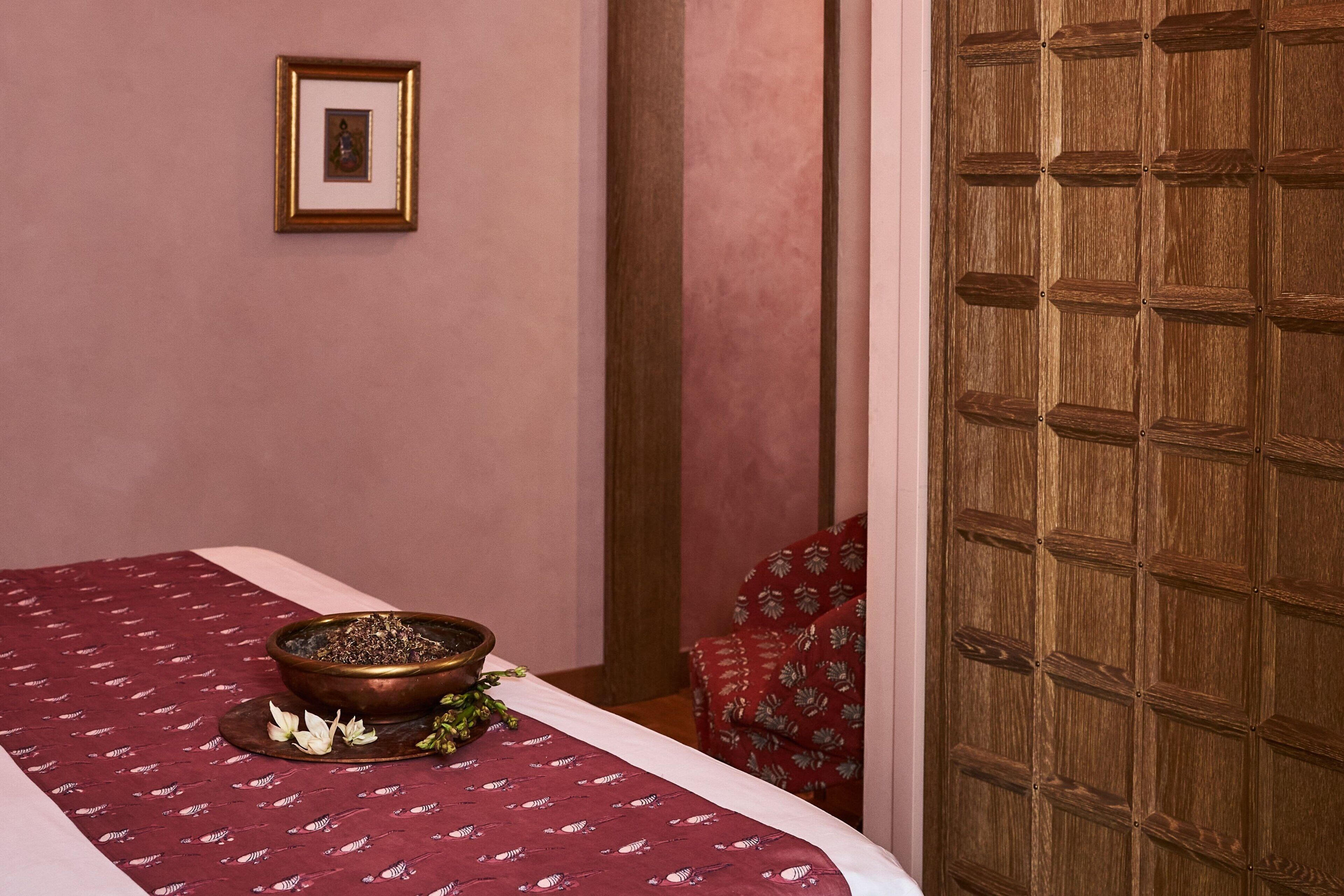 A room with a bed, a wooden door, a framed picture on the wall, and a decorative bowl on the bed.