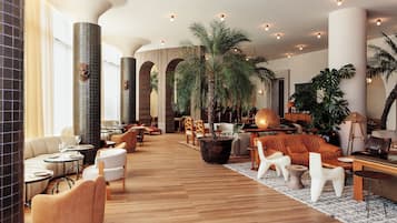 A spacious lobby with a wooden floor, multiple seating areas, and large potted plants.