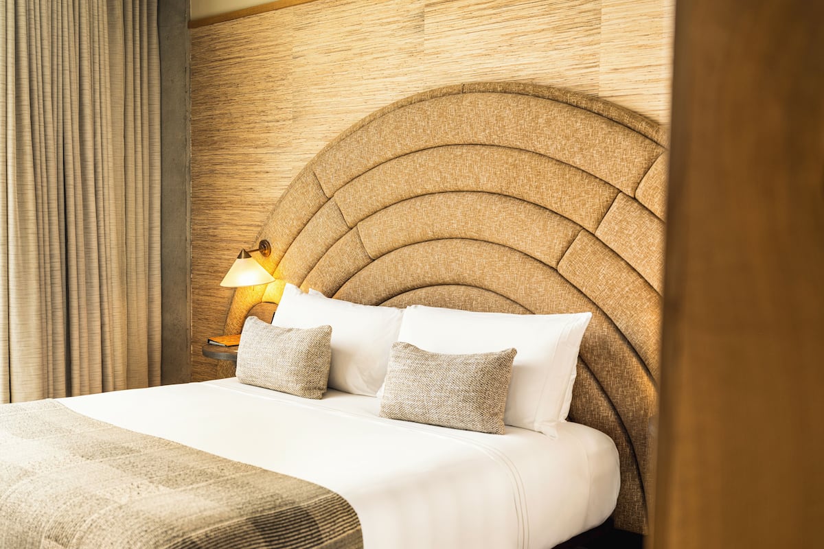 Una cama bien hecha con cabecera, almohadas y una lámpara de noche.