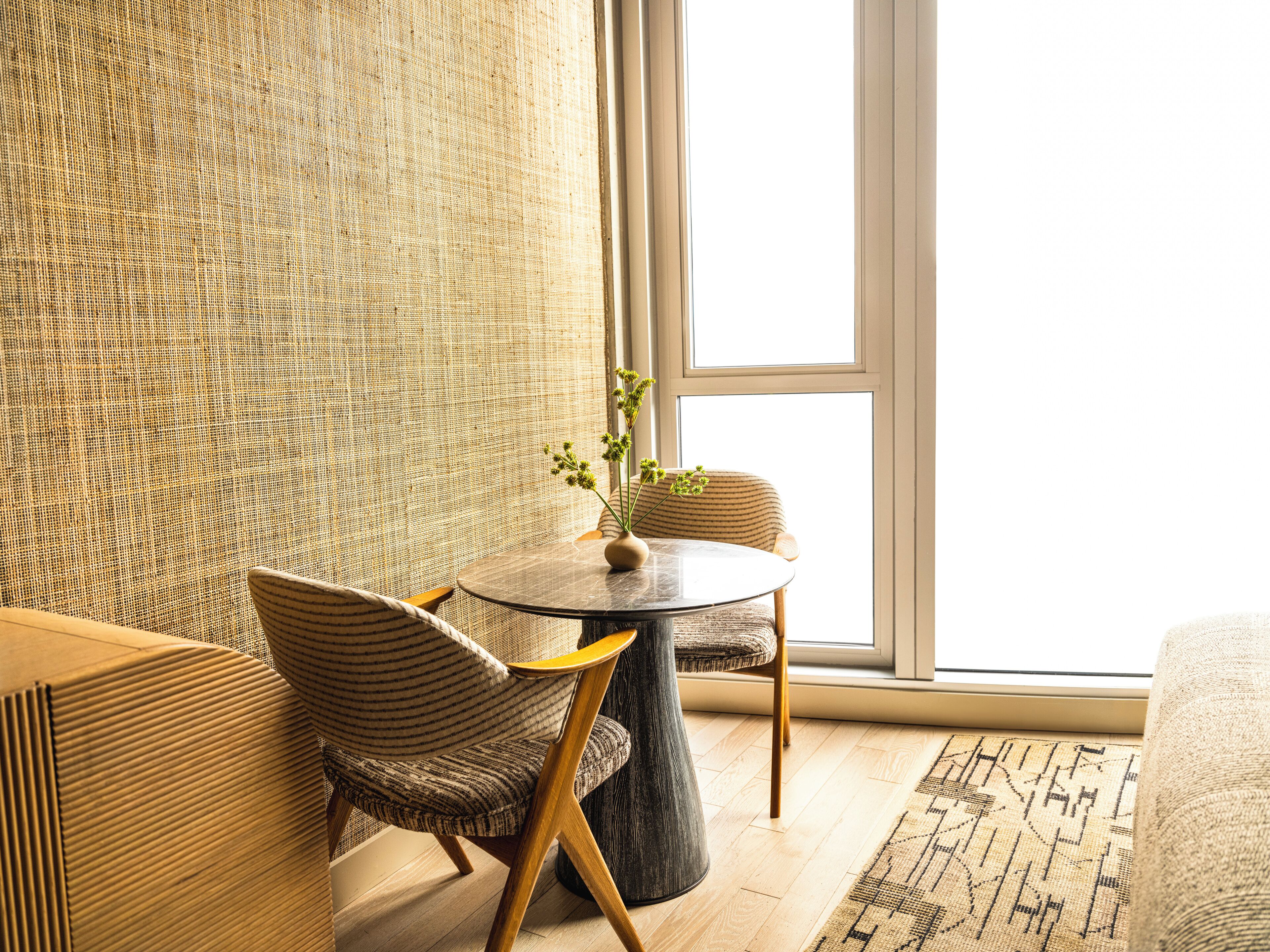 A modern living room with a round table, two striped chairs, a vase with flowers, and a large window.