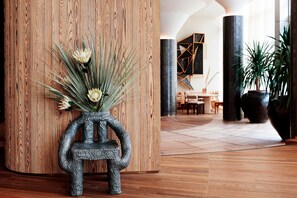 A modern lobby with a wooden column, a unique sculpture, and a dining area in the background.