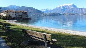 Une vue sur un lac, avec un banc, un bâtiment et des montagnes en arrière-plan.