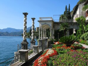 Ein Ufergarten mit Steinpfeilern, einem weißen Gazebo und bunten Blumen.