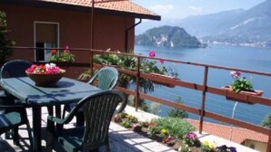 Une terrasse avec une table et des chaises, donnant sur un lac avec des montagnes en arrière-plan.