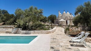 A stone pool with lounge chairs, surrounded by a stone wall and trees. - PRICKLY PEAR - Cone Life (Cisternino)