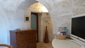 A room with a stone wall, a wooden cabinet, a television, and a wicker basket. - PRICKLY PEAR - Cone Life (Cisternino)