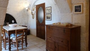 A room with a stone archway, a wooden dining table with chairs, a wooden cabinet, and a mirror. - PRICKLY PEAR - Cone Life (Cisternino)