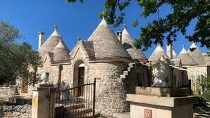 A stone building with multiple conical roofs, a gated entrance, and a mailbox. - PRICKLY PEAR - Cone Life (Cisternino)