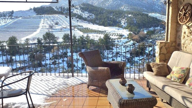 Un balcón con mobiliario de mimbre, un sofá y vistas a colinas nevadas.