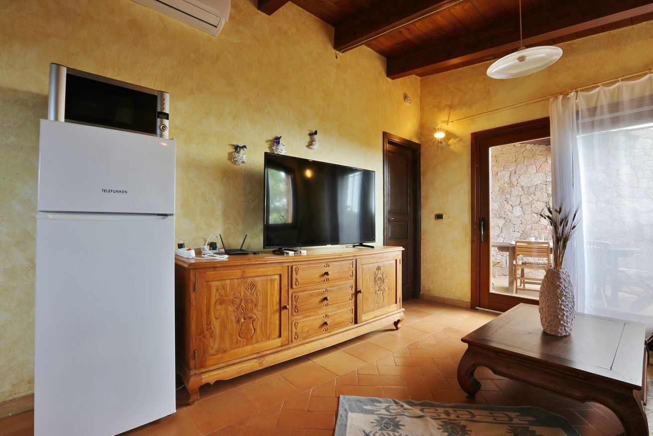 Un espace de vie compact comprenant un réfrigérateur blanc, un meuble en bois, un téléviseur à écran plat et un coin repas avec une table et un vase.