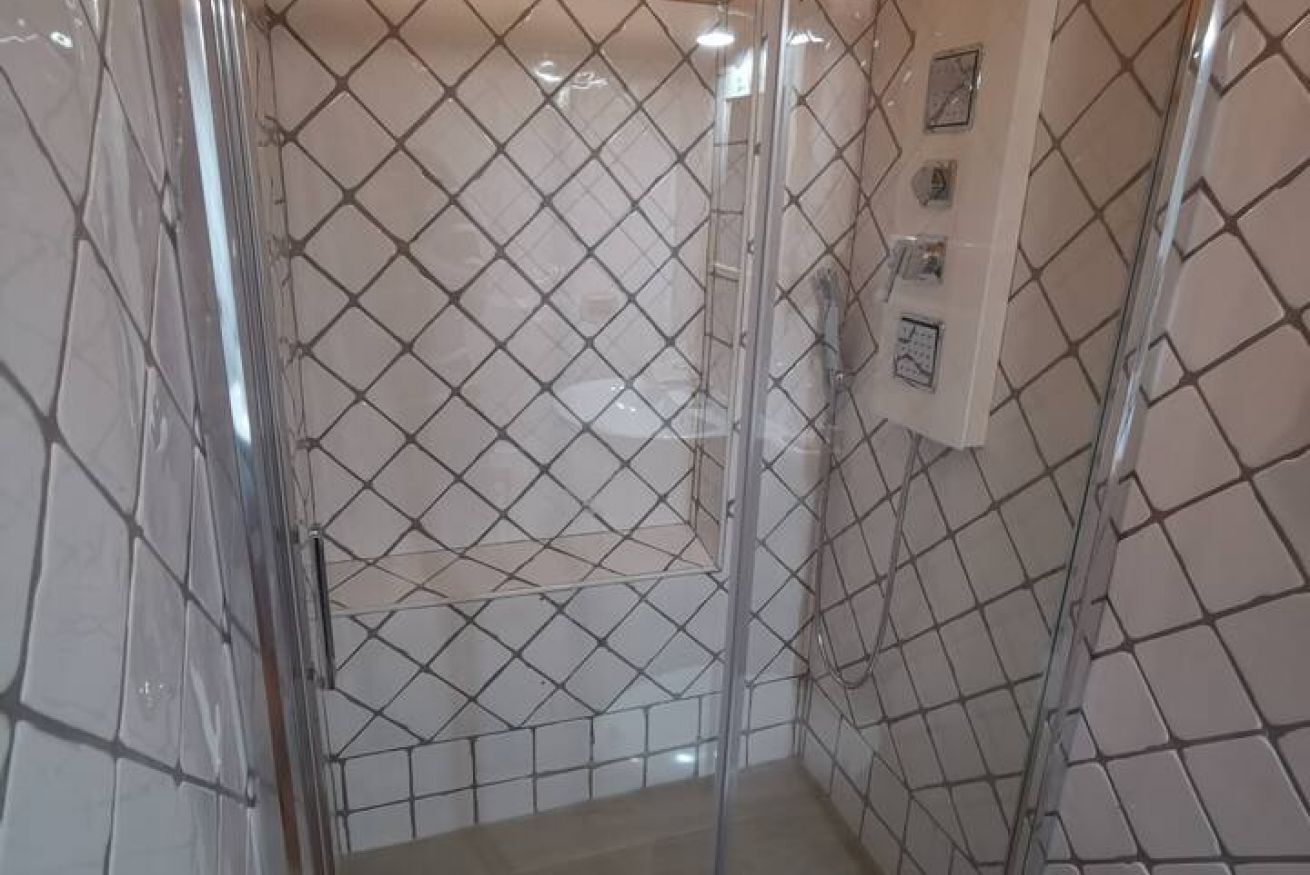 Une cabine de douche carrelée avec une porte en verre et une barre d’appui.