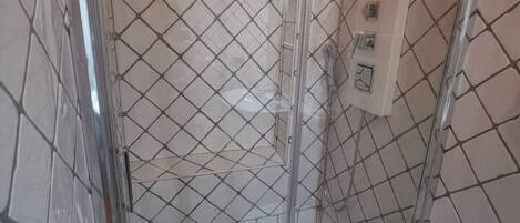 Une cabine de douche carrelée avec une porte en verre et une barre d’appui.