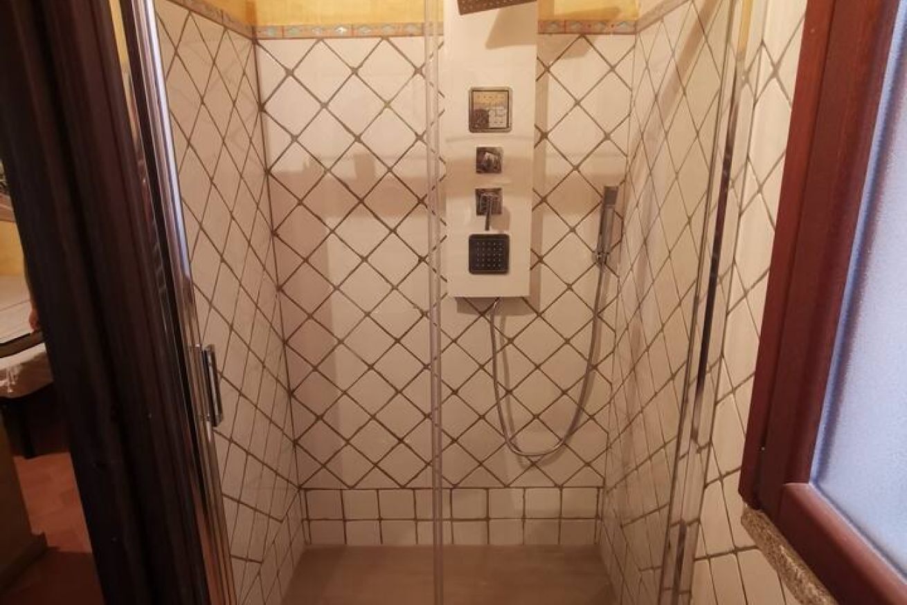 Une petite salle de bain carrelée, équipée d’une douche et d’un panneau de commande.