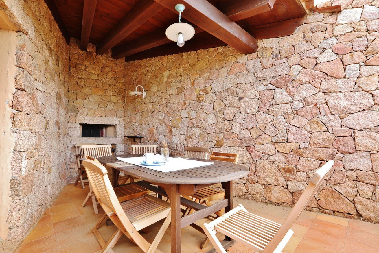 Un área de comedor al aire libre con paredes de piedra, una mesa y sillas de madera, una chimenea de piedra y un techo de madera.