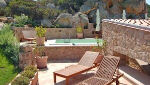 A stone-walled outdoor area with a pool, lounge chairs, and potted plants.