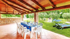 An outdoor covered patio with a table set for dining, surrounded by chairs, and a lawn with lounge chairs. - Villa Il Casolare Country House with pool (Itri)