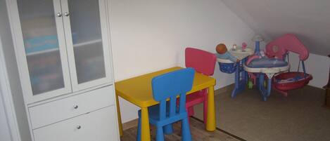Ein Zimmer mit Holzboden, einem weißen Schrank mit Milchglasschränken, einem gelb-blauen Stuhl, einem kleinen Tisch und einem Spieltisch für Kinder mit Spüle und Spielzeug.