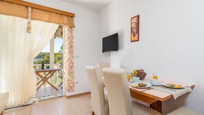 Ein Essbereich mit einem für zwei Personen gedecktem Tisch, einem an der Wand montierten Fernseher und einem Balkon mit Vorhängen.