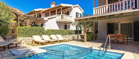 A pool area with lounge chairs, a wooden deck, and a stone wall.