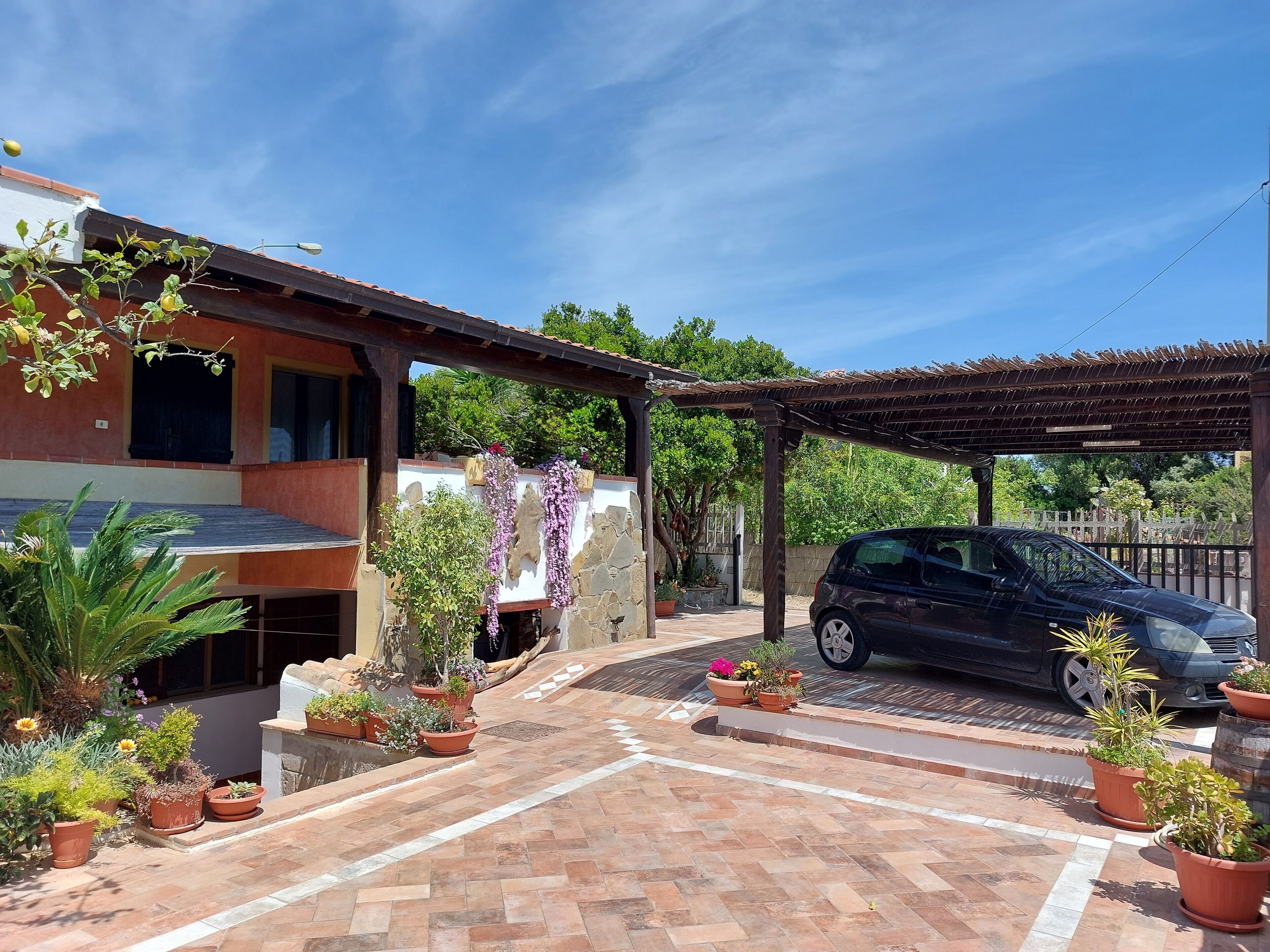 Una casa con porche cubierto, plantas en macetas y un coche aparcado.
