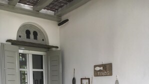 Ein Zimmer mit einer weißen Tür, einem weißen Regal mit Dekorationsobjekten, einem Steinboden und einem grauen Eimer mit Pflanzgefäßen.