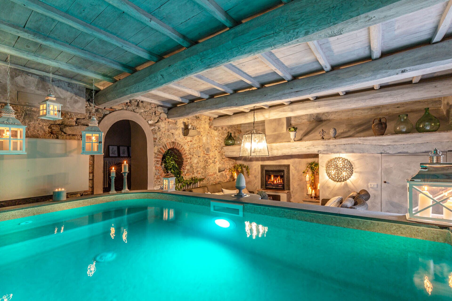 A pool area with a stone wall, a fireplace, and hanging lanterns.