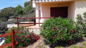 Un bâtiment à la façade en pierre, doté d’un portail en bois et d’un jardin agrémenté de fleurs rouges.