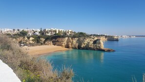 Una zona costera con una playa de arena, mar azul cristalino y edificios en un acantilado.