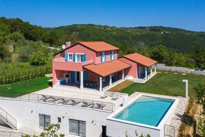 A modern two-story house with a swimming pool, surrounded by a well-maintained lawn and a forested hillside. - New Property with Heated Pool near Bike Trails and Truffle Capital of Istria (Oprtalj)