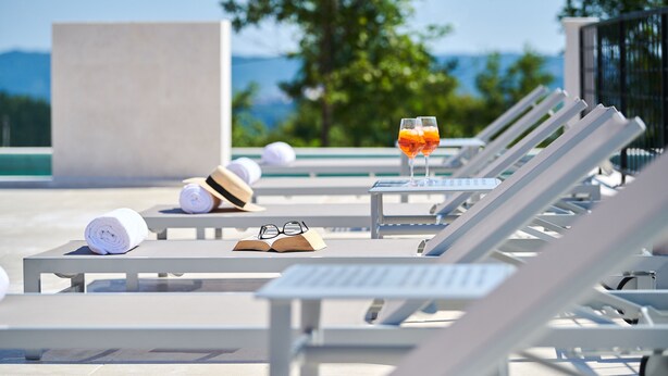 A poolside lounge area with sun loungers, a glass of orange juice, a book, and rolled towels. - New Property with Heated Pool near Bike Trails and Truffle Capital of Istria (Oprtalj)