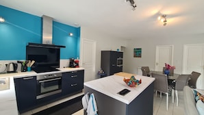 Une cuisine moderne avec un mur d’accent bleu, un îlot central et un coin repas comprenant une table et des chaises.