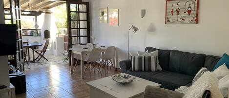 A living room with a sofa, a coffee table, a dining table with chairs, a TV, and a fireplace.