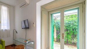 A room with a glass table, a television, a wicker basket, and a sliding glass door leading to a garden.