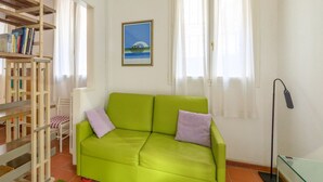 A room with a green sofa, a bookshelf, a framed picture, and a window with curtains.