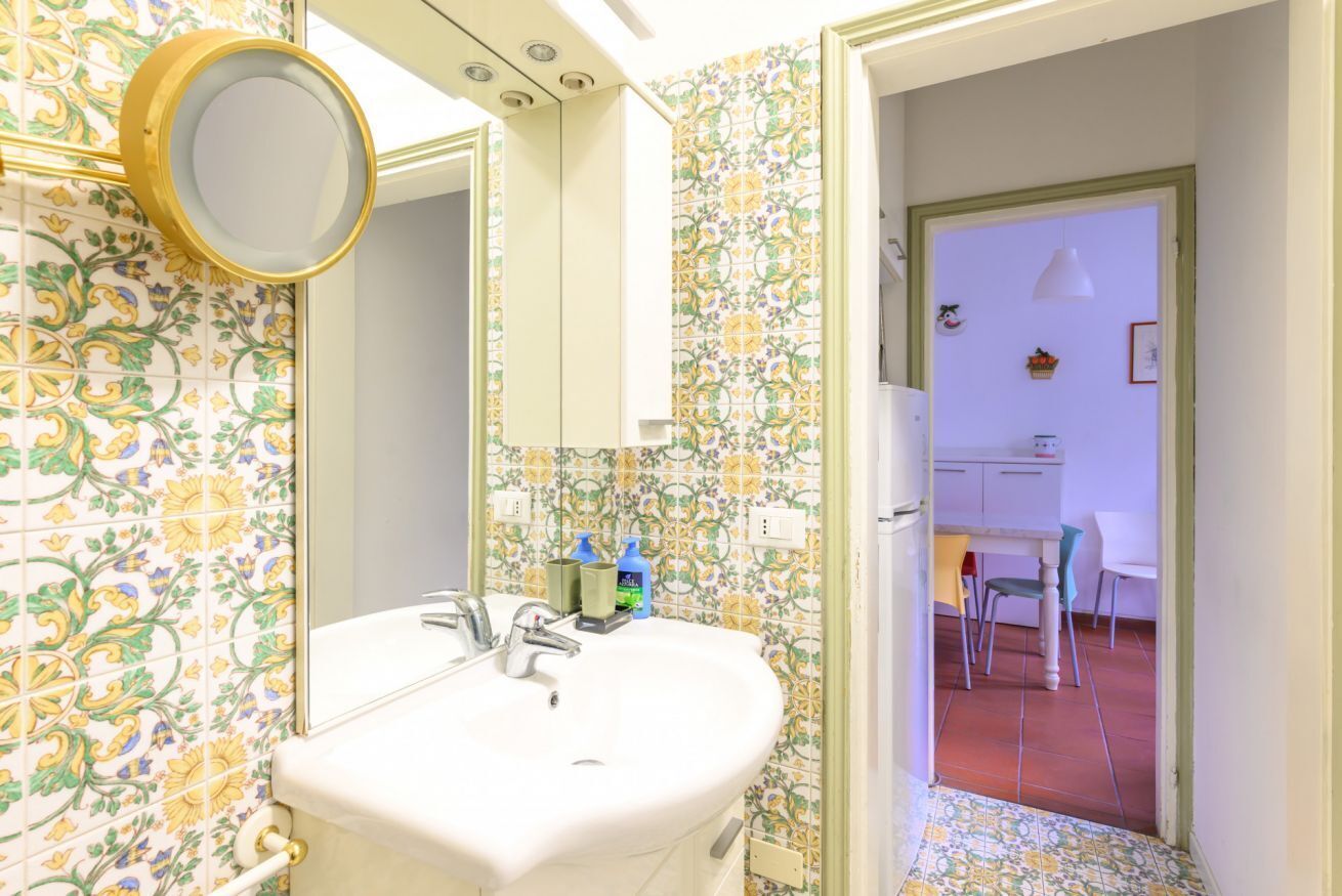 Un baño con lavamanos, espejo y paredes con azulejos.