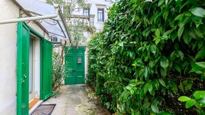 A narrow alleyway with a green door, a metal awning, and a dense hedge.