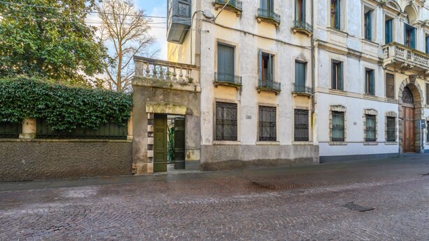 A historic building with a cobblestone street, a wrought iron gate, and a stone wall with greenery.
