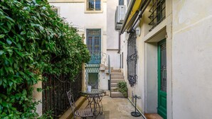 A narrow courtyard with a metal table and chair, a green door, and a staircase leading to an upper level.