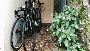 A narrow alleyway with a wooden door, two bicycles, and a clock on the wall.