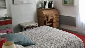 A bedroom with a bed, a wooden dresser, a mirror, and a wall-mounted shelf with glassware.