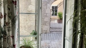 A room with a view of a courtyard through a glass door. There is a small stool with a potted plant on it.