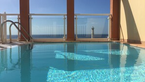 Una piscina amb aigua cristal·lina, una escala metàl·lica i vista a l'oceà a través de grans finestres.
