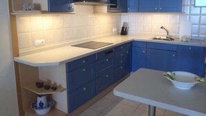 Una cuina moderna amb armaris blaus, un taulell blanc i un forn de microones integrat.