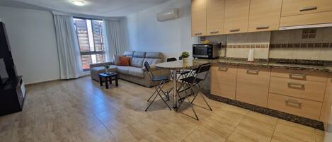 A compact living space with a kitchenette, a sofa, a dining table with chairs, and a window with blinds.